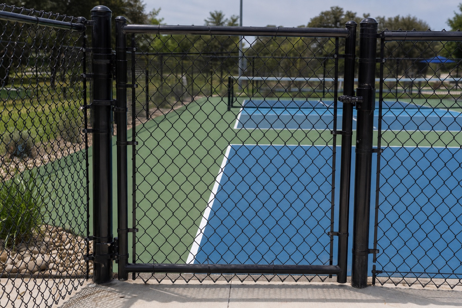 A black chain-link gate opening onto a blue and green pickleball court