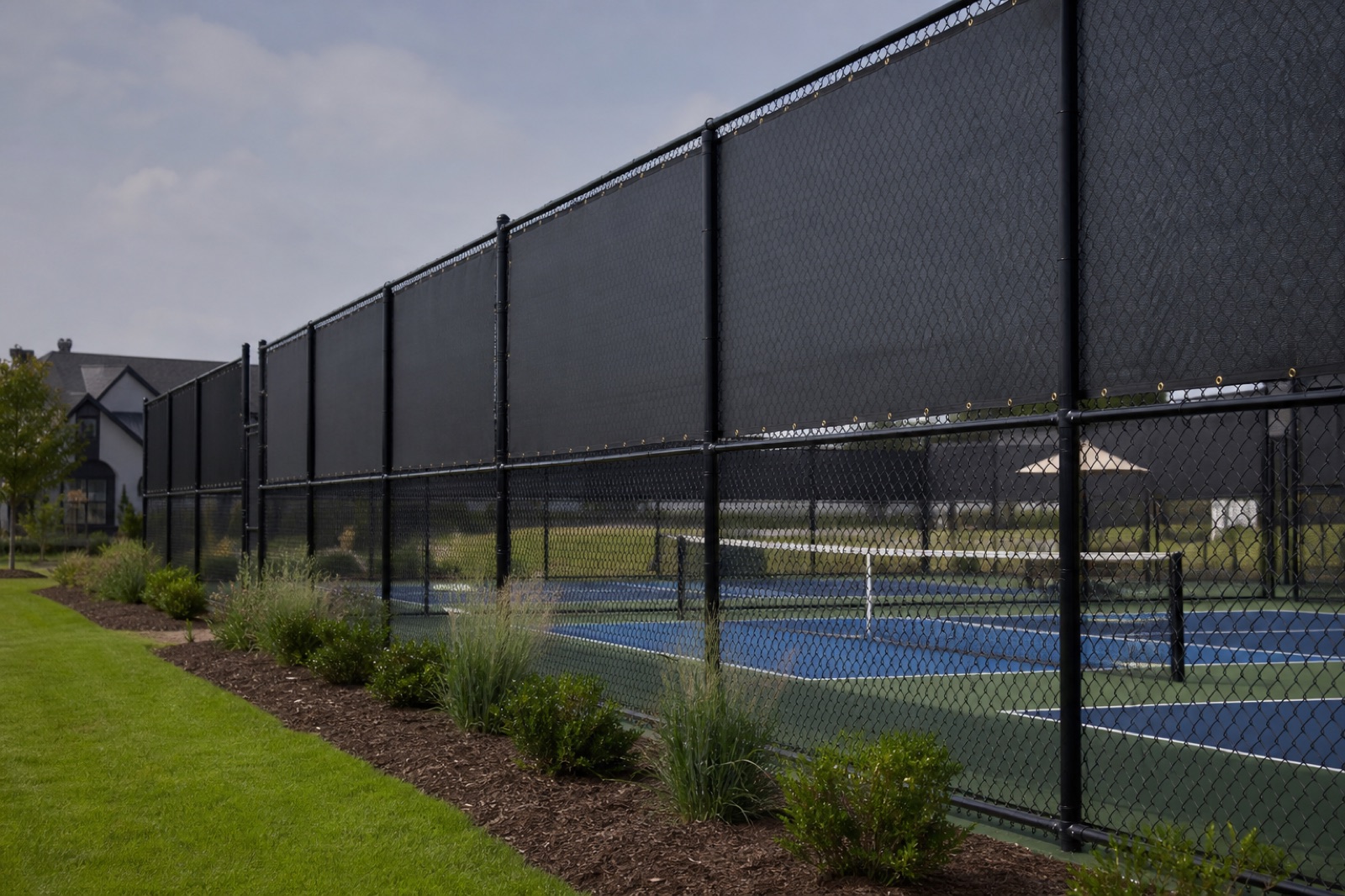 Dark coated pickleball court fencing fitted with windscreens