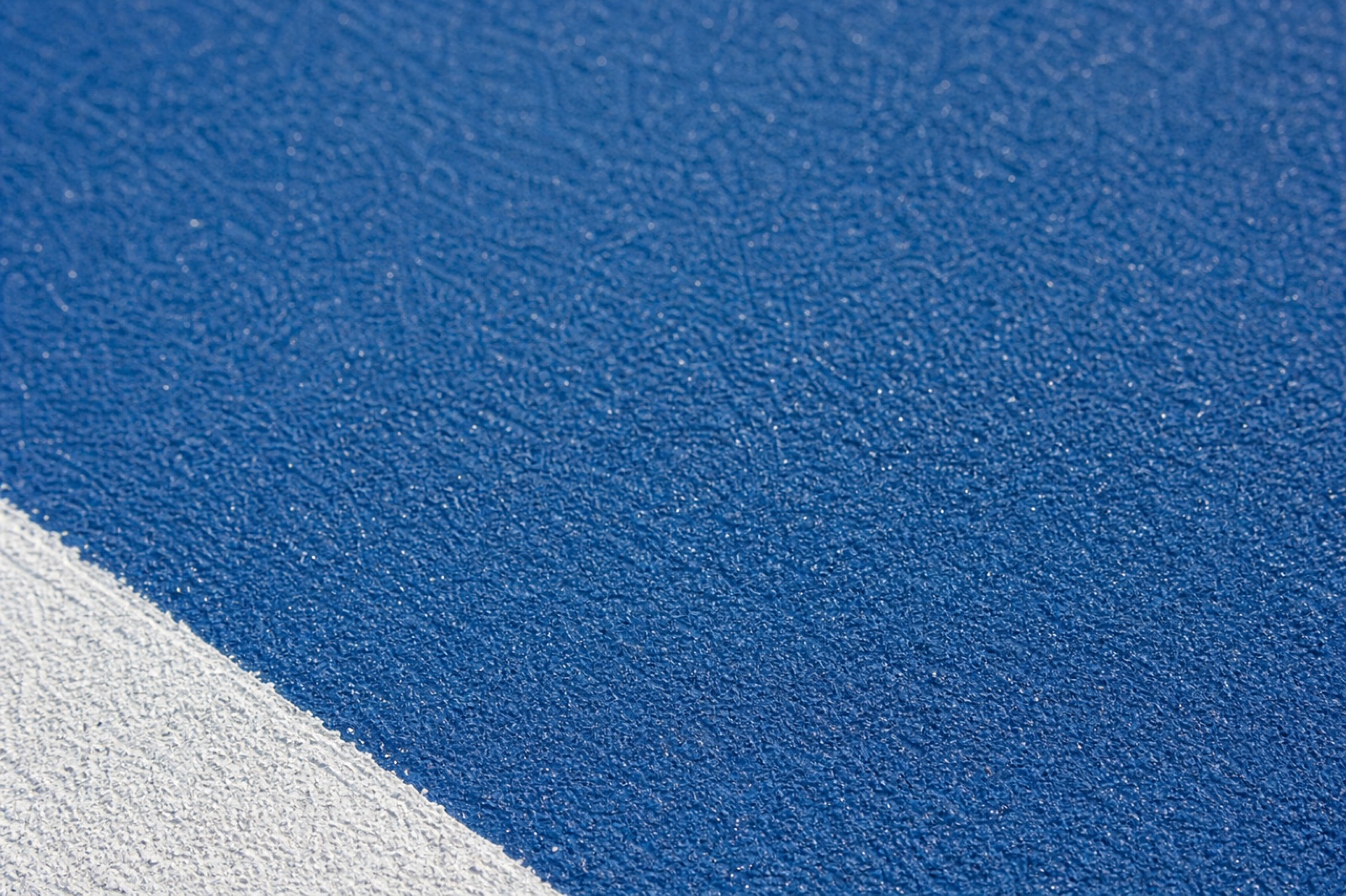 Close view of textured blue acrylic court surfacing beside a white line
