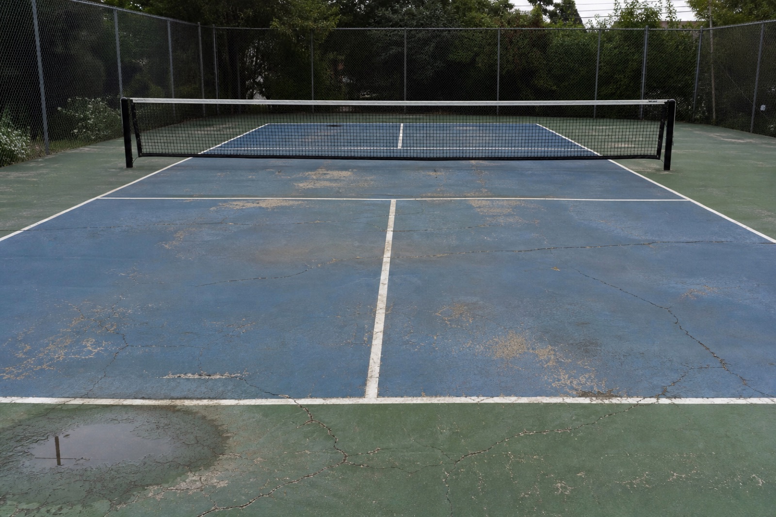 Worn court with cracks, fading, and a low area holding water